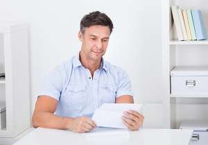 Smiling man reading a letter at a bright white desk, stock photo